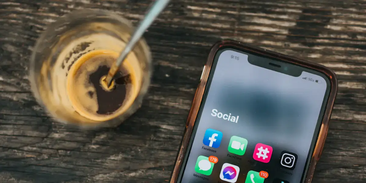 Teléfono móvil con iconos de redes sociales junto a un café sobre madera