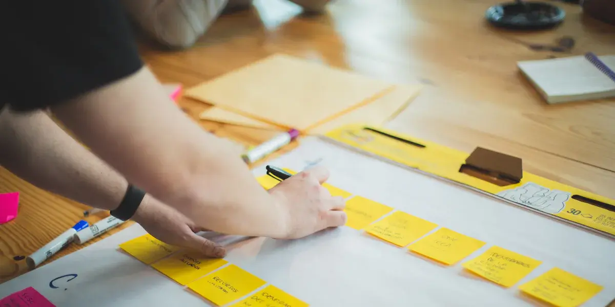 Persona trabajando con papeles y notas de color sobre una mesa de madera
